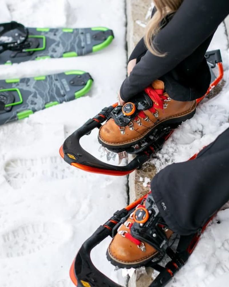 Person strapping into snowshoes with hiking boots on packed snow