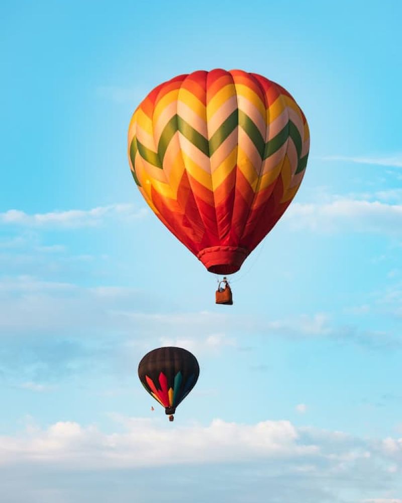 Two hot air balloons floating at different heights against a cloud-dotted sky