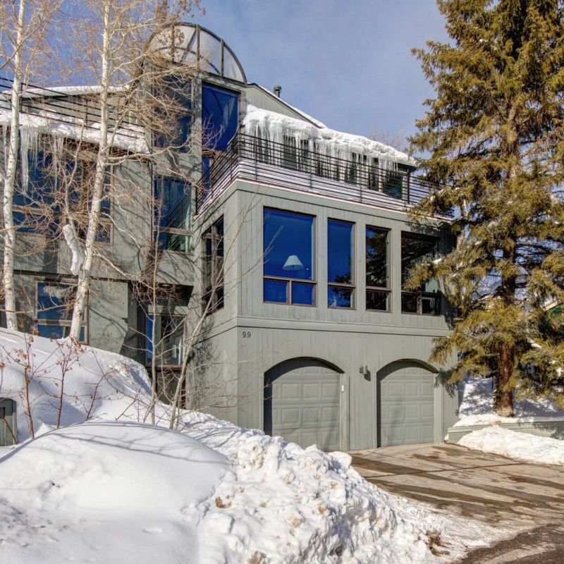 Three-story mountain home exterior with snow-covered driveway and aspens