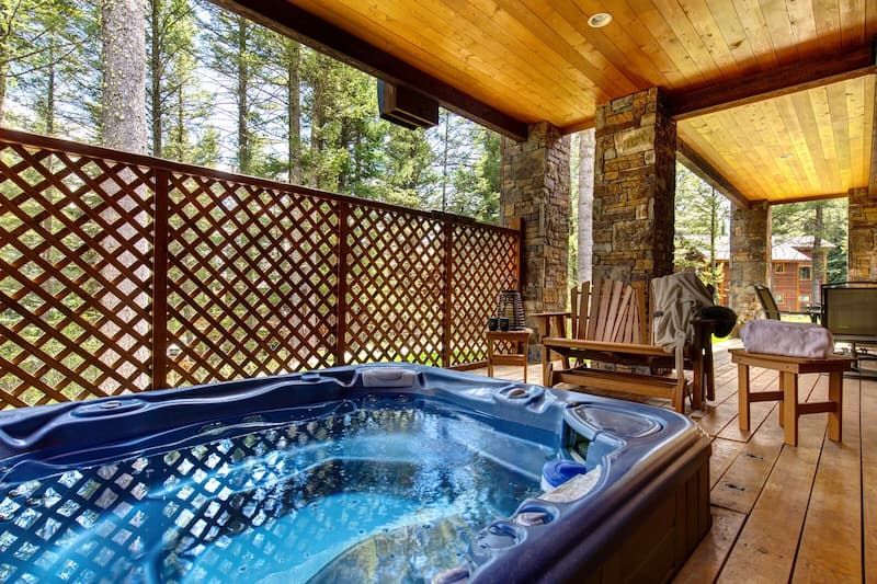 Outdoor hot tub on a covered wooden deck surrounded by tall evergreen trees