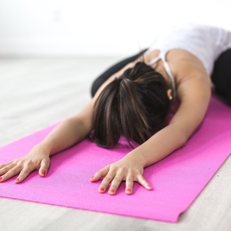 Woman in child's pose stretching on a pink yoga mat