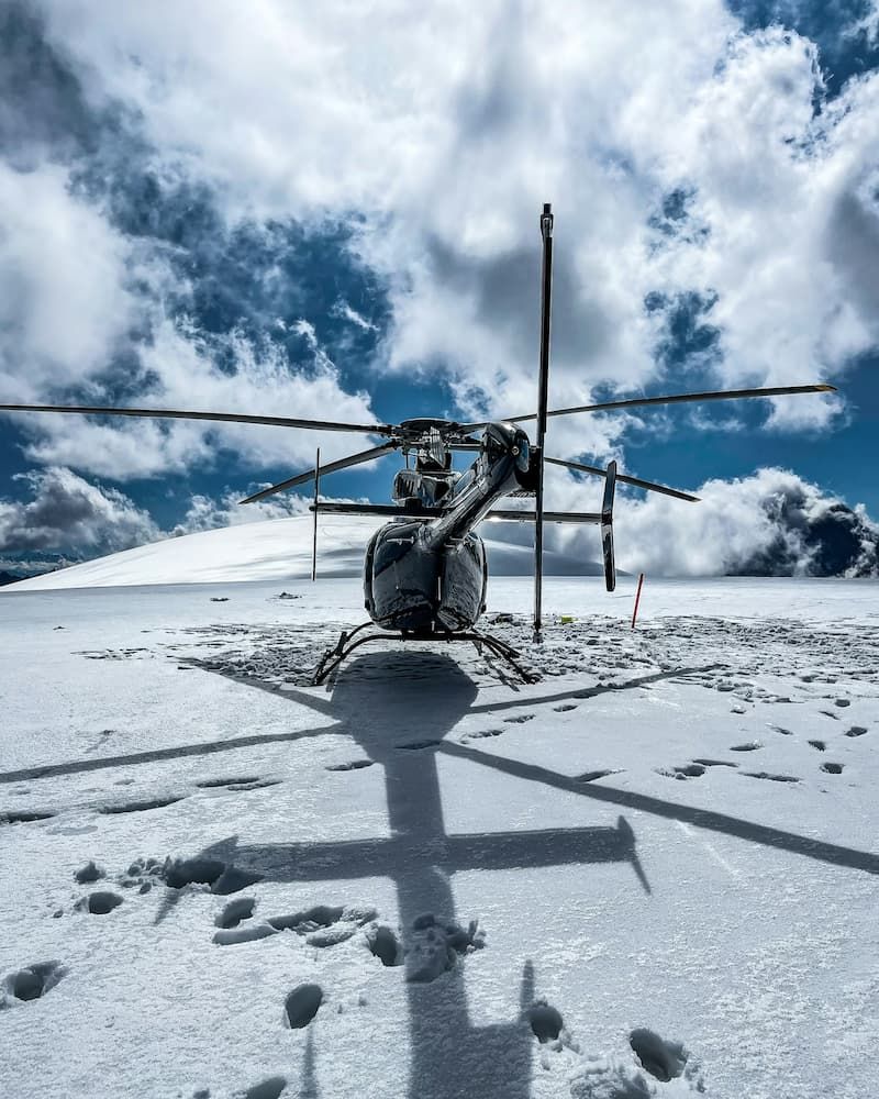 Helicopter parked on a snow-covered mountain ridge under cloudy sky