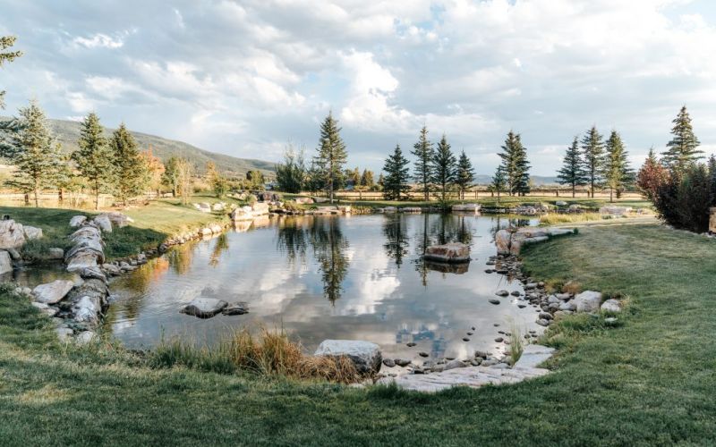 Reflective pond surrounded by evergreens and rolling hills at twilight