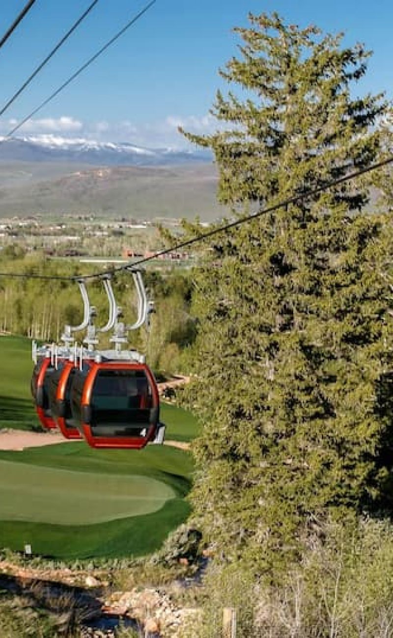 Red gondola cabins crossing a fairway with Park City valley views