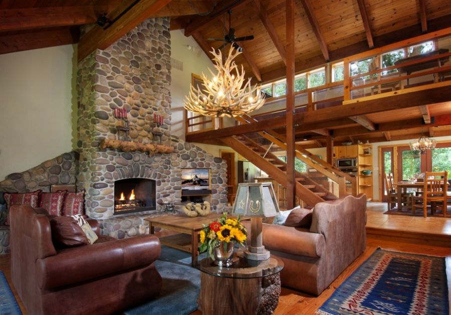 Great room with river-rock fireplace, antler chandelier, and timber loft
