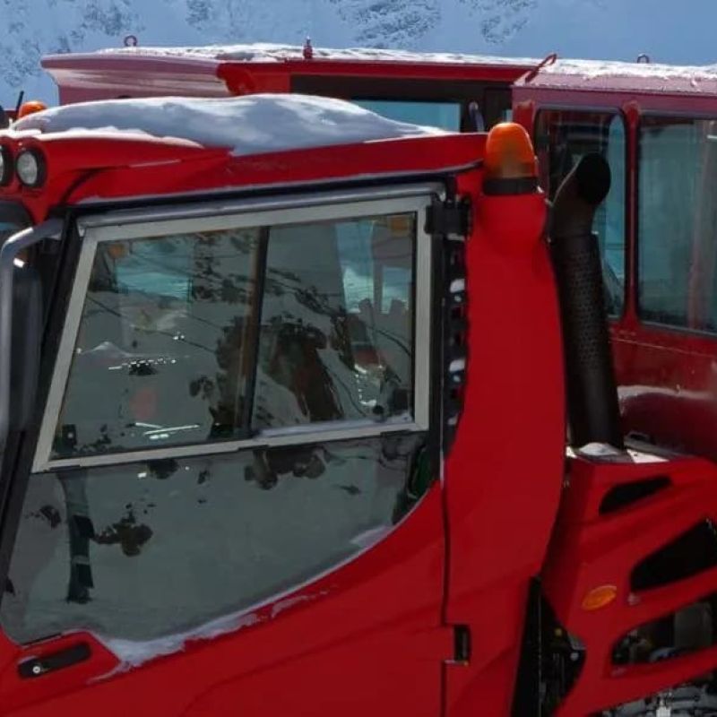 Red snowcat groomers parked in front of snowy mountains