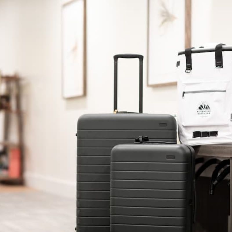 Two rolling suitcases and an Adventure Awaits cooler backpack in an entryway