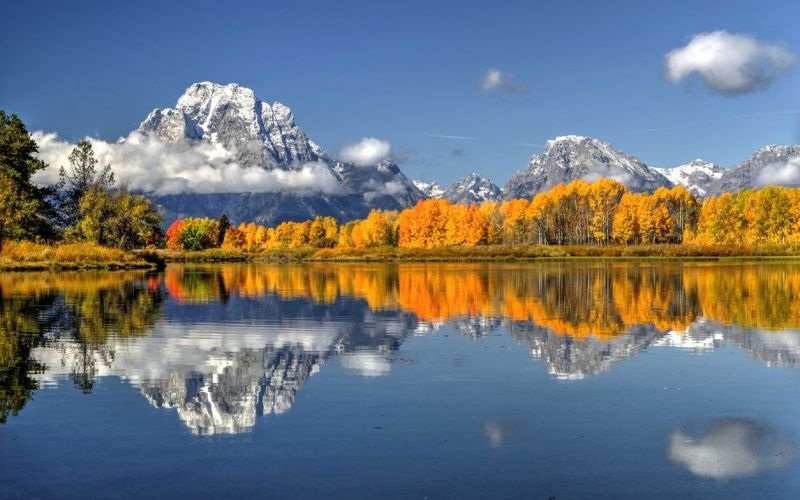 Snow-dusted Teton peaks reflected in a still lake bordered by golden aspens