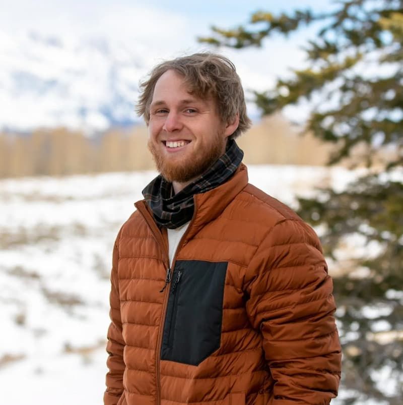 Smiling young man in orange puffer jacket and flannel scarf outdoors in winter