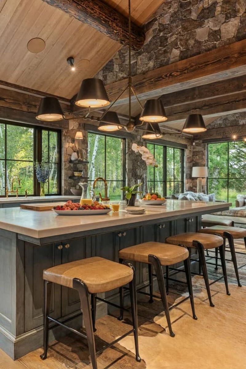 Rustic kitchen with stone walls, vaulted wood ceiling, and large island with stools