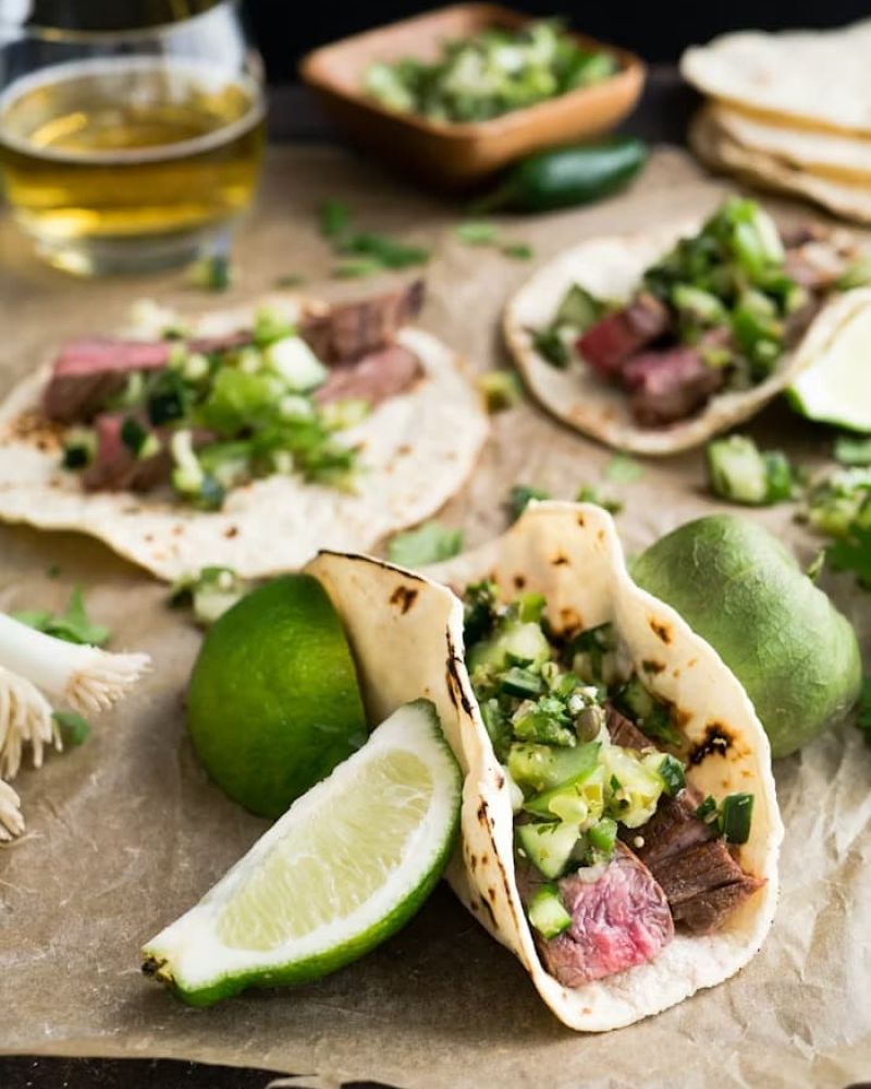 Skirt steak street tacos topped with cucumber salsa and lime wedges