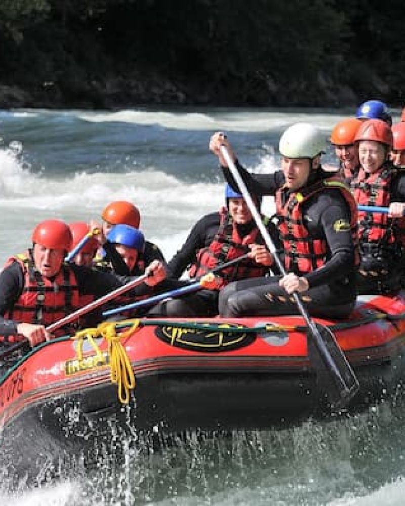 Group of helmeted rafters paddling a red whitewater raft through river rapids