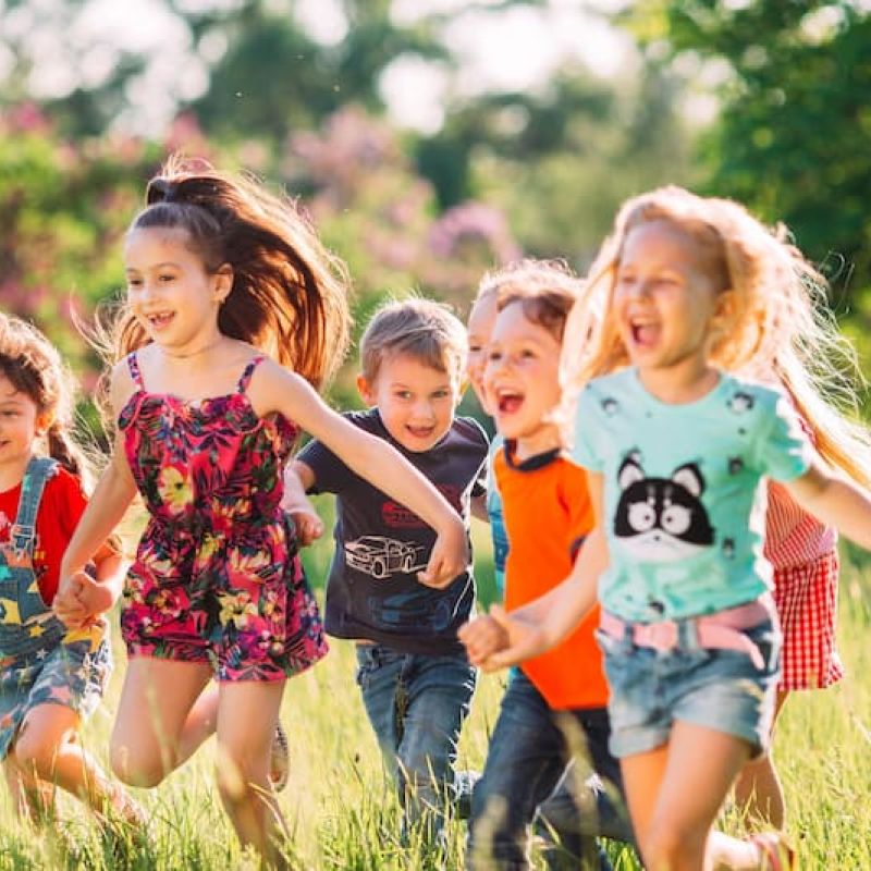 Group of children running together through a sunlit grassy field