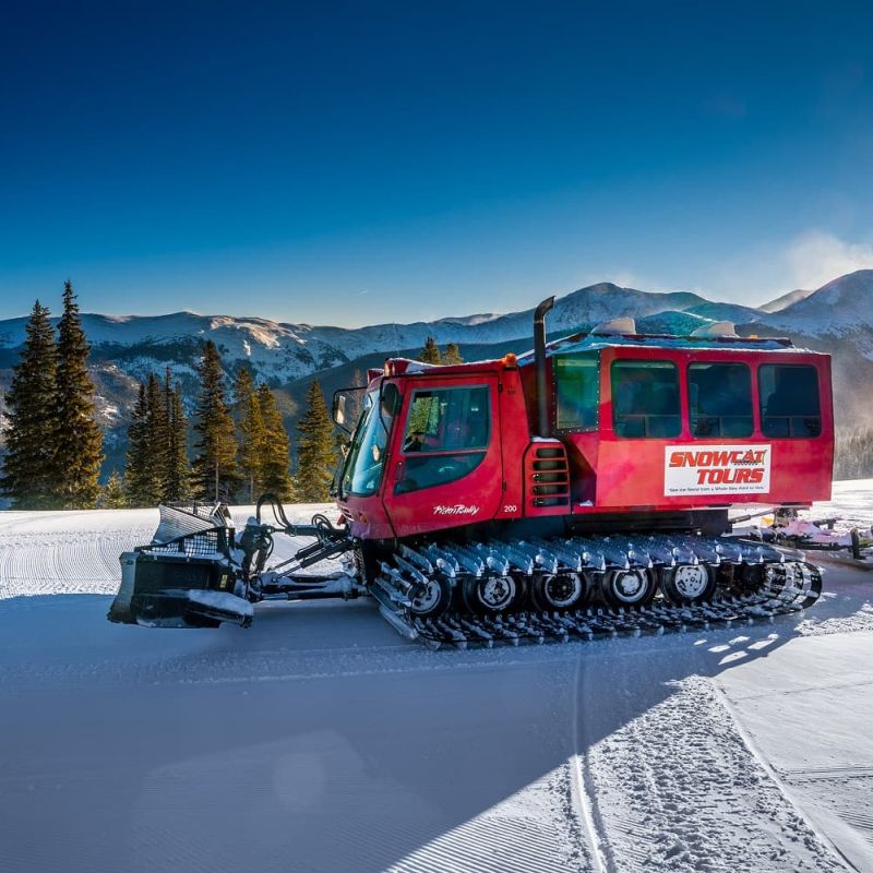 Red Snowcat Tours vehicle parked on groomed snow with mountain backdrop