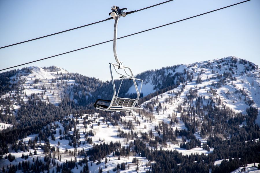 Empty ski chairlift suspended above snow-covered mountain slopes and pines
