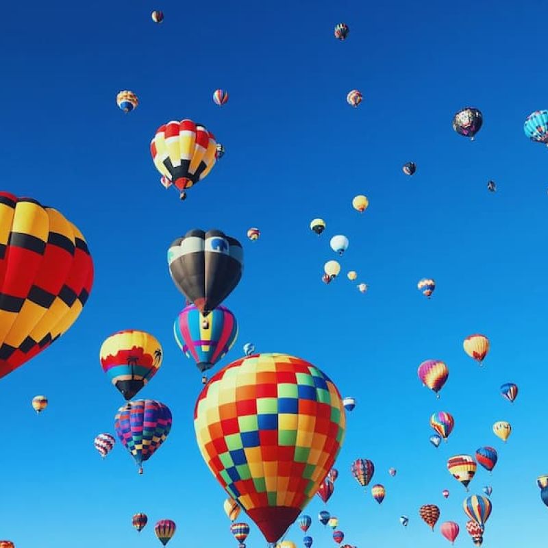 Dozens of colorful hot air balloons floating against a deep blue sky