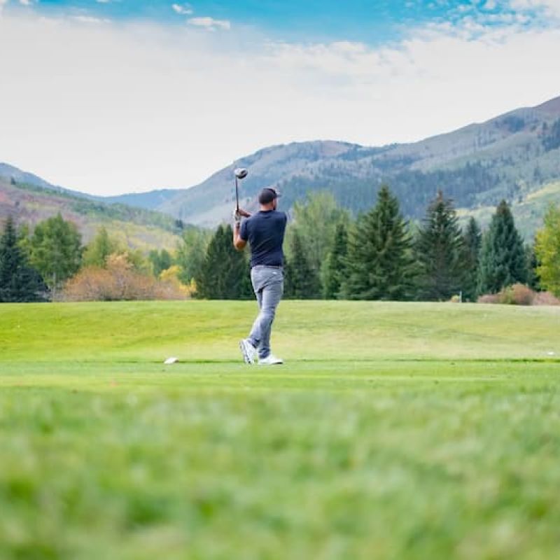 Golfer finishing a tee shot on a fairway framed by mountains