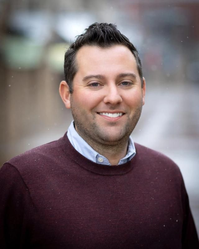 Headshot of a smiling man in a maroon sweater with snow falling