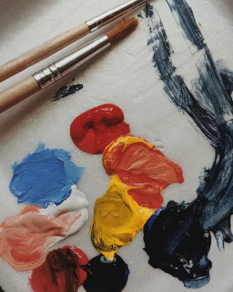Artist palette with red, yellow, blue, and navy paint dollops and two brushes