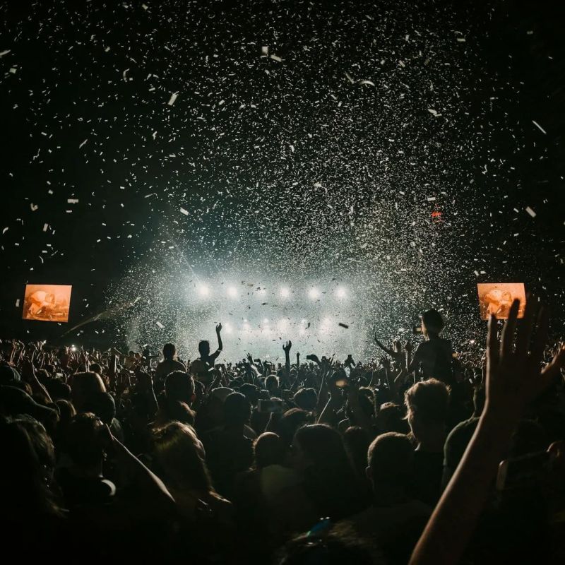 Concert crowd with raised hands as confetti rains over a lit stage