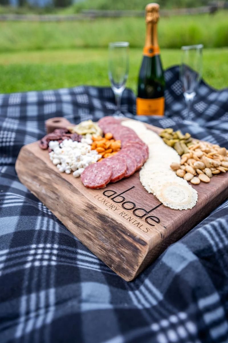 Charcuterie board branded Abode Luxury Rentals with champagne on a picnic blanket