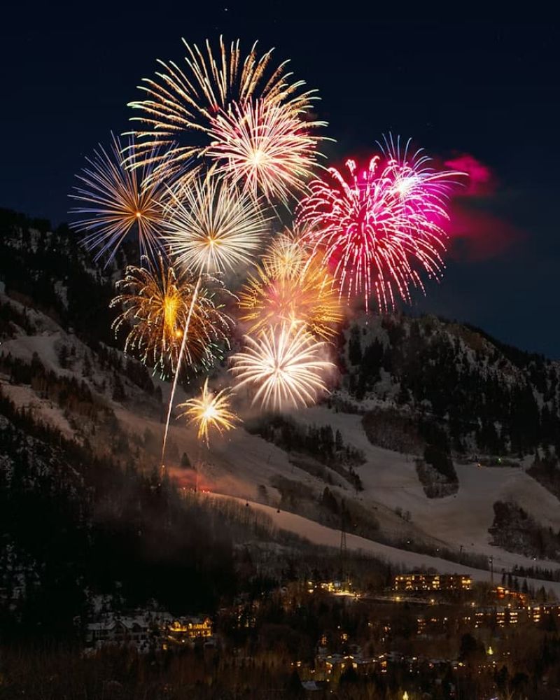 Fireworks bursting over a snowy ski mountain above a town at night