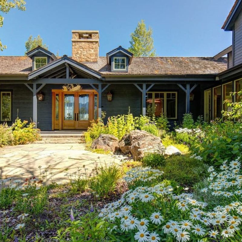 Dark wood mountain home exterior with stone chimney and wildflower garden