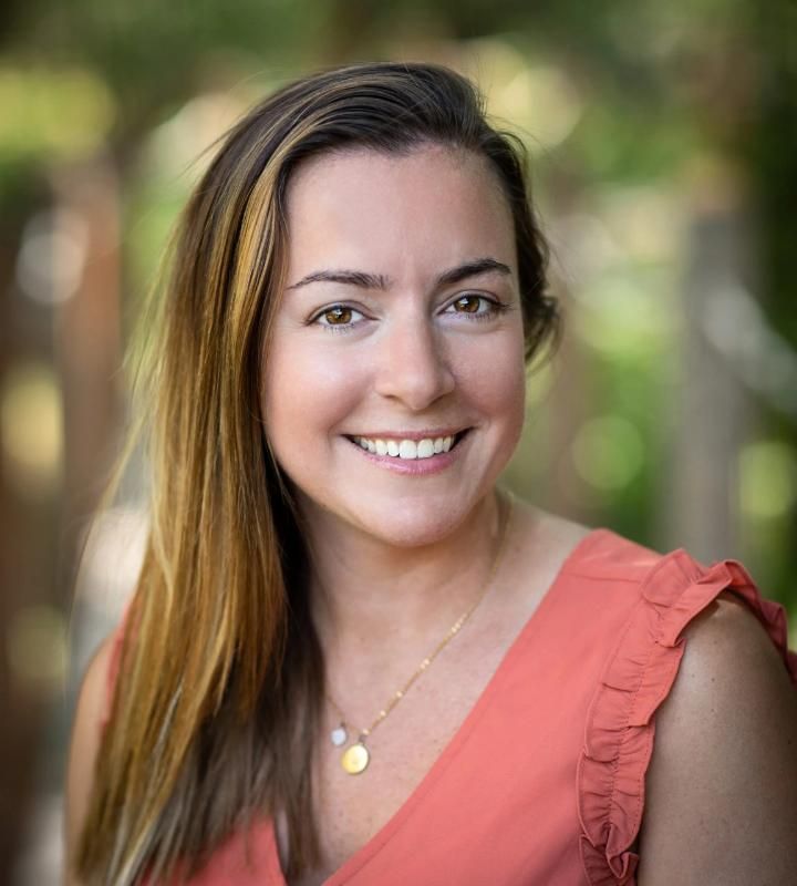 Headshot of a smiling woman in a coral sleeveless top