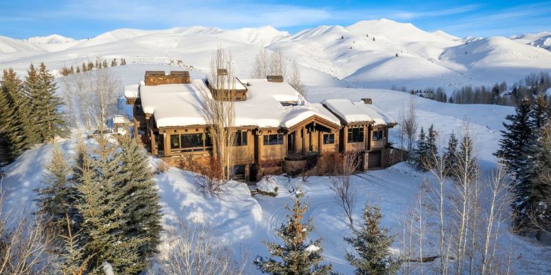 Aerial view of a mountain home blanketed in snow with peaks behind