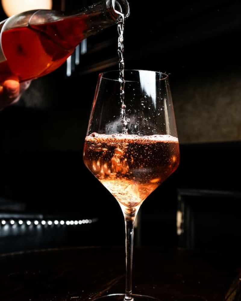 Rose wine being poured into a tall stemmed glass on a dark bar top