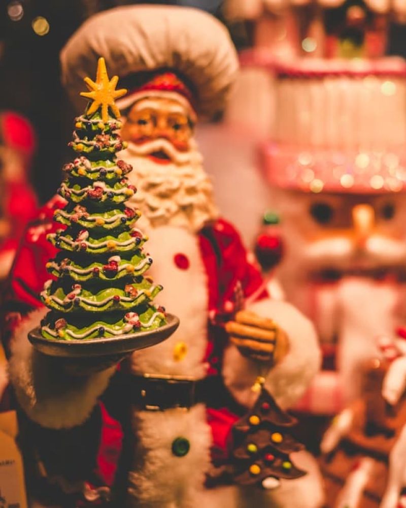 Festive Santa figurine holding a green Christmas tree among holiday decorations