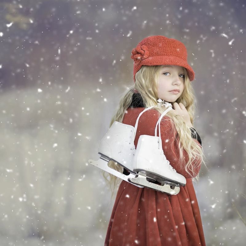 Young girl in red coat holding white ice skates during snowfall