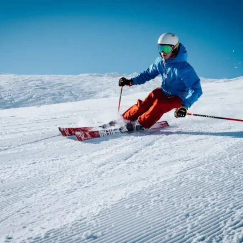 Skier in blue jacket carving a turn down a groomed slope