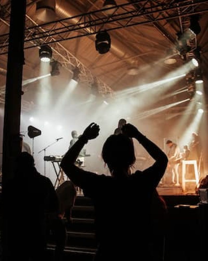 Concert crowd with raised hands silhouetted against stage lights and haze