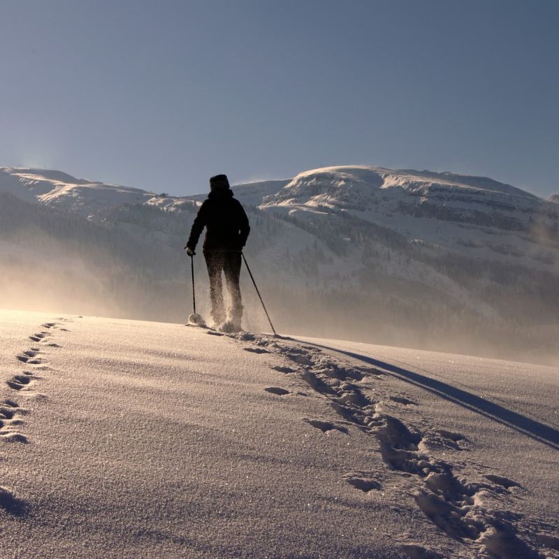 Snowshoer crossing a high snowfield toward distant peaks at sunrise
