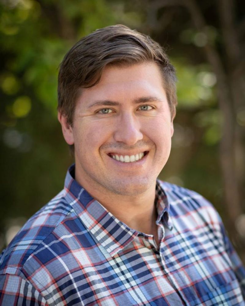 Headshot of a smiling man in a blue plaid shirt