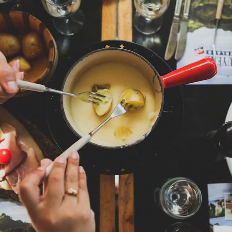 Overhead view of two diners sharing a cheese fondue with charcuterie and salad