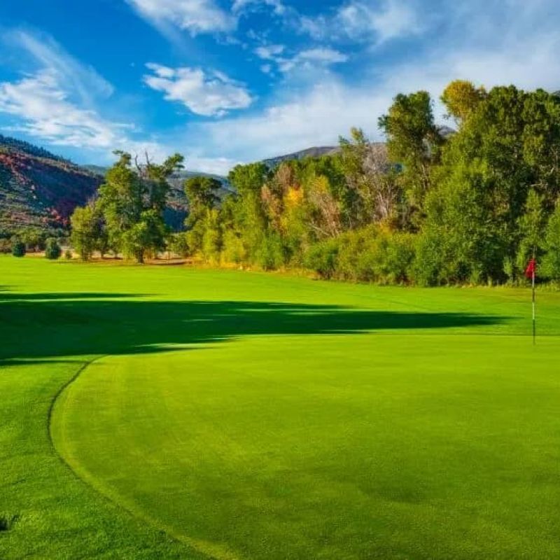 Manicured fairway and green with a red flag and mountain backdrop