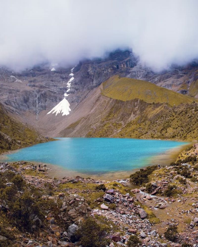 Turquoise alpine lake beneath cloud-shrouded snow-capped peaks