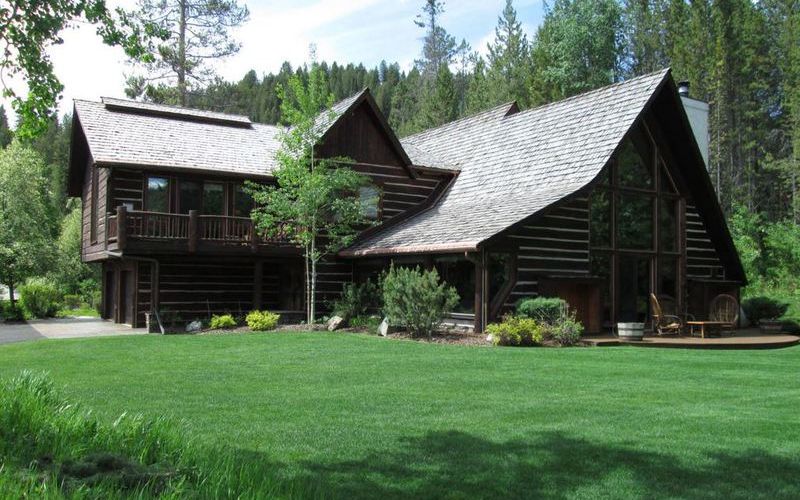 Log cabin with steep cedar-shingle roof set on a green lawn