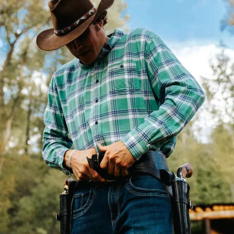 Cowboy in plaid shirt and hat fastening a holster outdoors