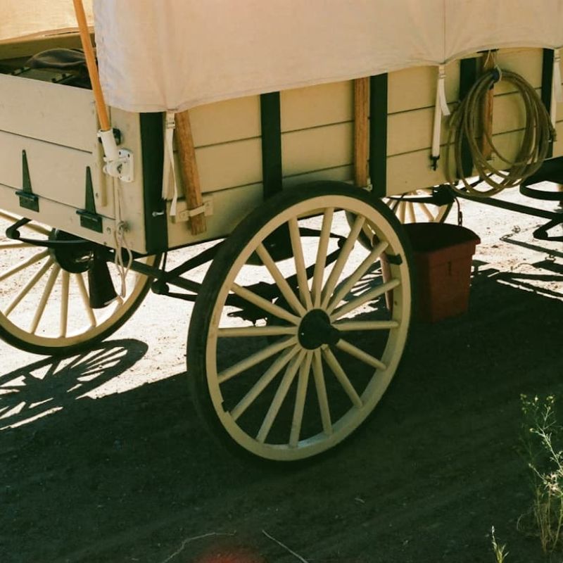 Restored covered wagon with wooden spoked wheels parked on a dirt path