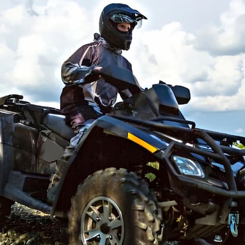 Rider on a black ATV navigating muddy terrain in a helmet and goggles
