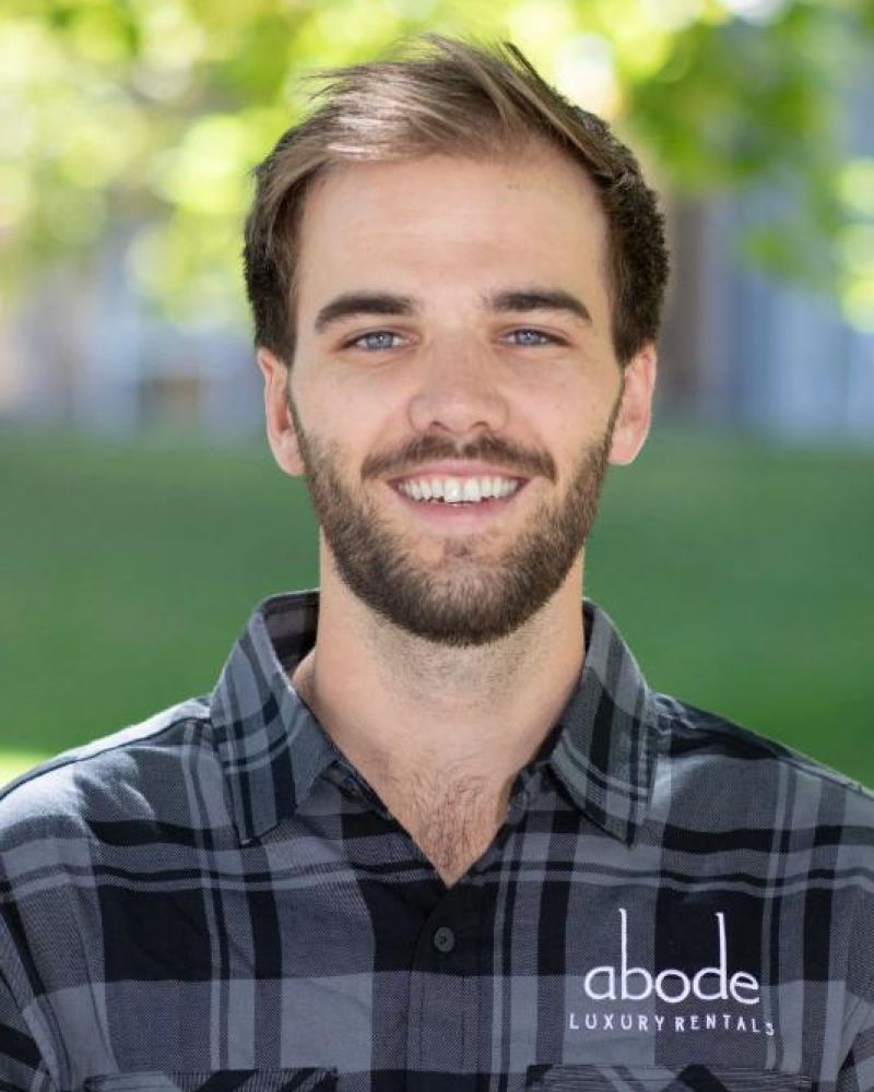 Smiling man wearing a gray plaid Abode Luxury Rentals shirt