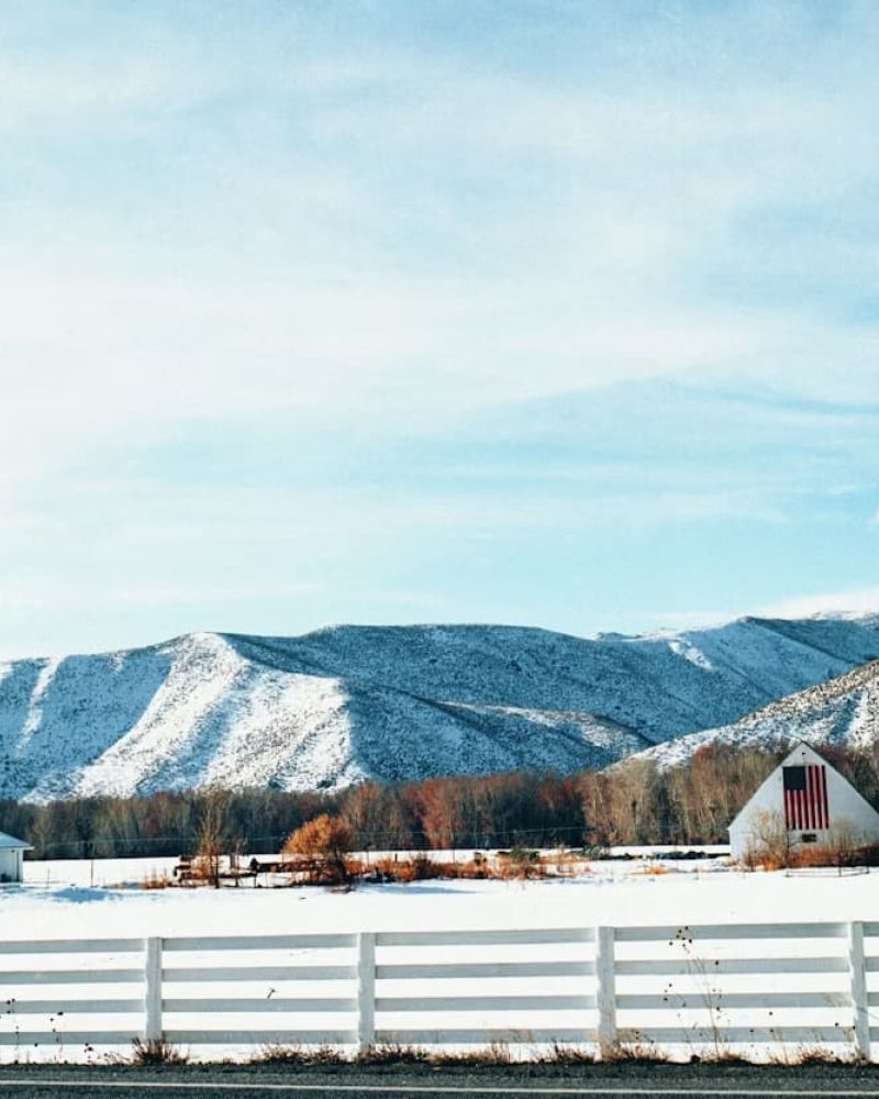White barn with a large American flag below snow-dusted Sun Valley hills