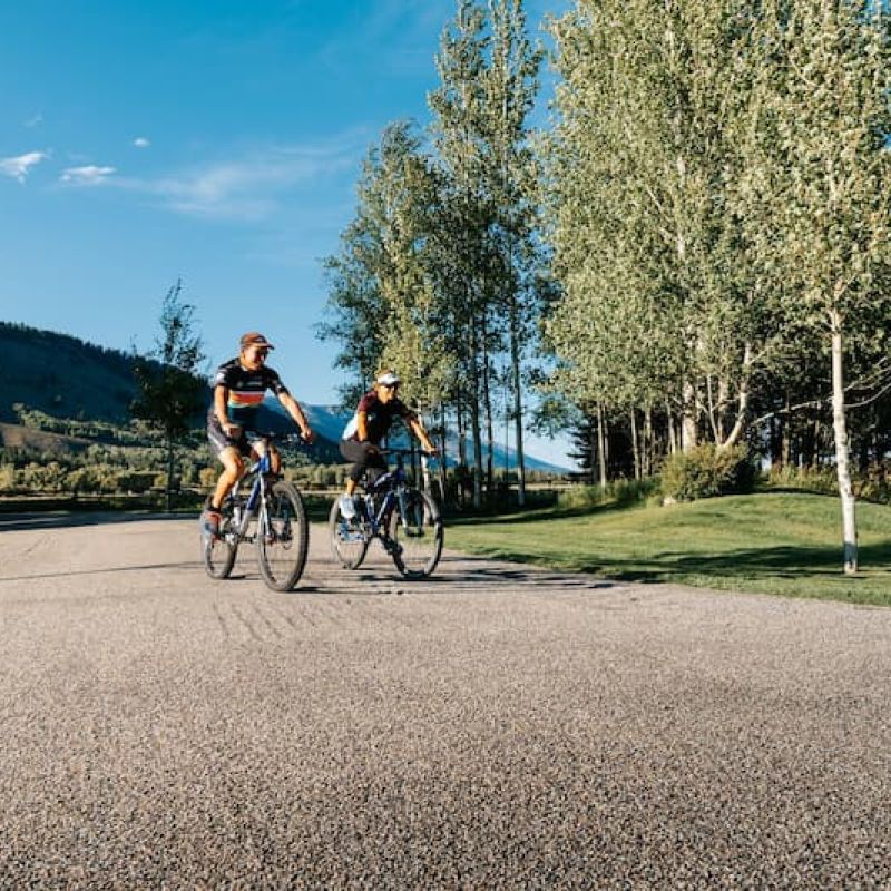 Two cyclists riding a paved path with mountain backdrop in Jackson Hole