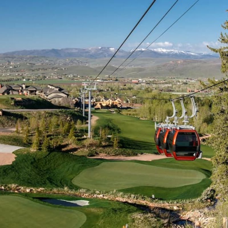 Red gondola cabins crossing a fairway with Park City valley views