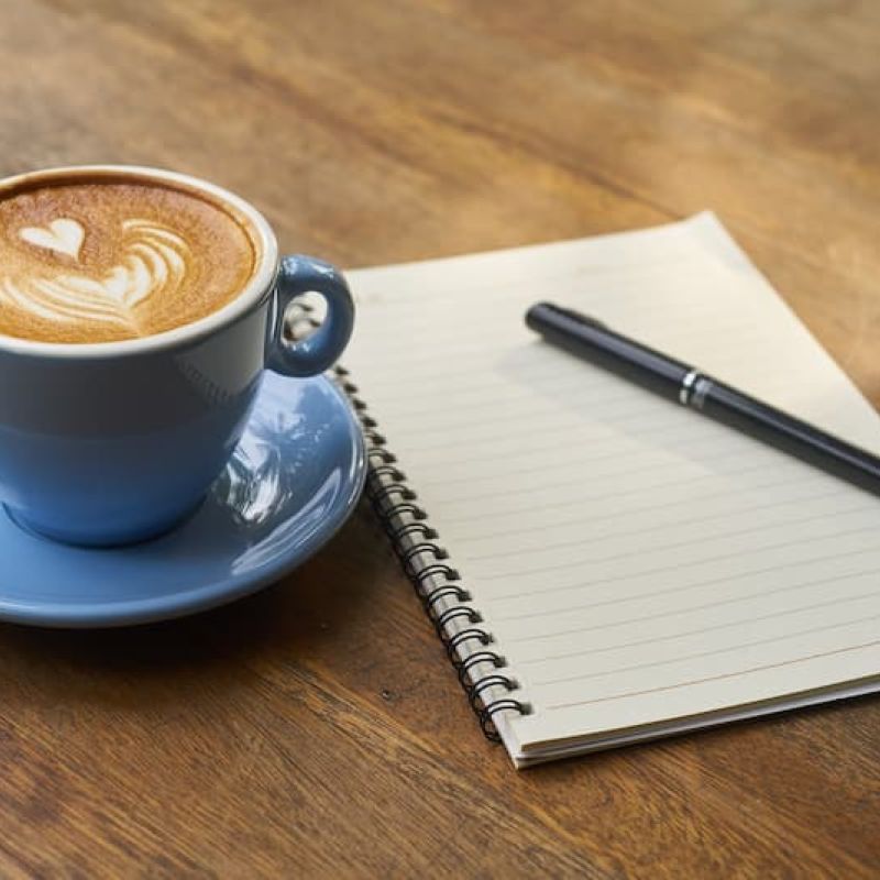 Latte with heart art beside an open notebook and pen