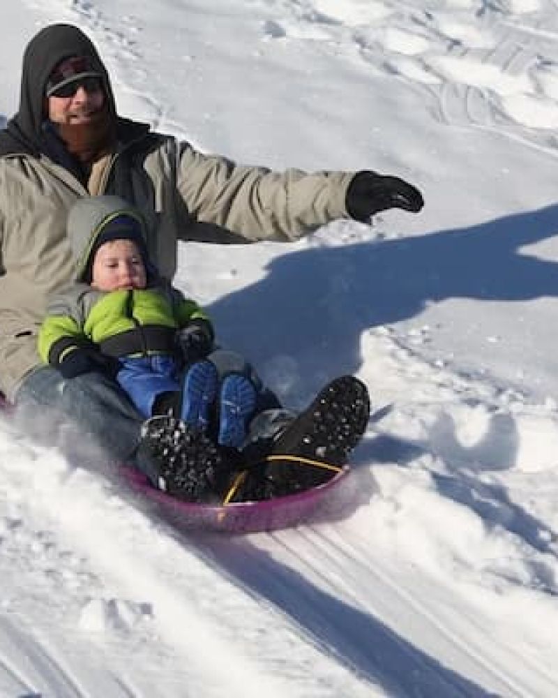 Adult and toddler riding a snow tube down a packed sledding hill