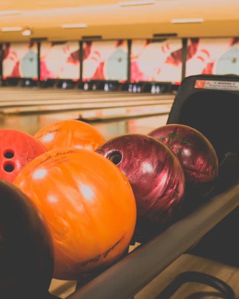 Colorful bowling balls lined up in a return rack beside the lanes